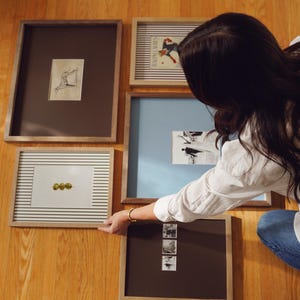 K&ouml;nnte beinhalten: Eine Sammlung gerahmter Kunstwerke in verschiedenen Gr&ouml;&szlig;en und Stilen. Die Rahmen sind in Braun- und Naturholzt&ouml;nen gehalten. Die Kunstwerke umfassen Zeichnungen und Illustrationen. Die St&uuml;cke sind auf einer Holzoberfl&auml;che angeordnet.