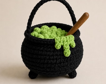 May include: A black crocheted cauldron with a handle and three small feet. The cauldron is filled with textured light green crocheted spheres, with a light green crocheted drip over the rim and a single wooden stirring stick inserted inside.