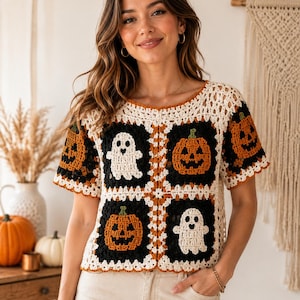 May include: A short-sleeved crochet top featuring a granny square pattern with alternating black squares containing white ghost motifs and orange pumpkin designs, bordered by cream-colored yarn with a scalloped edge and a round neckline.