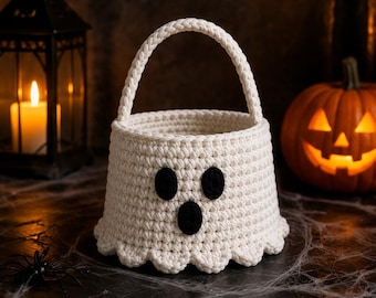 May include: A cream-colored crocheted basket shaped like a ghost, featuring a braided handle and three black felt-like circles forming eyes and a mouth. The base of the basket has a scalloped edge, creating a rounded, ghost-like silhouette.