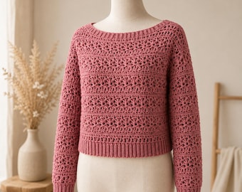 May include: A dusty rose long-sleeve sweater featuring a repeating crochet pattern with horizontal bands of openwork floral motifs, a wide boat neckline, and ribbed cuffs and hem, displayed on a mannequin torso.