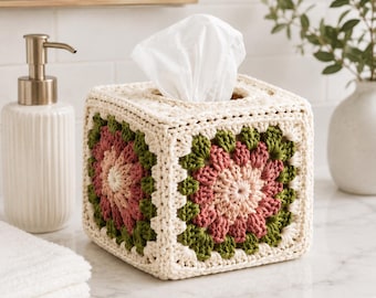 May include: A square tissue box cover featuring a crochet granny square pattern in cream, olive green, and dusty rose yarn. The cover is constructed with a thick, textured yarn and has an open top to allow white facial tissues to be pulled through.