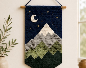 May include: A rectangular crochet wall hanging featuring a mountain landscape at night. The design includes a dark blue sky with a white crescent moon and gold embroidered stars, above layered mountains in white, gray, light green, and dark green.