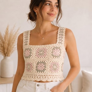 May include: A sleeveless crochet top featuring a square neckline and wide straps. The garment is constructed from multiple granny square motifs in a color palette of cream, soft pink, and sage green, finished with a scalloped edge at the hem.