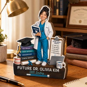 May include: A wooden desk ornament featuring a cartoon dental student in blue scrubs and a white coat, holding a book. It includes a stack of books, a graduation cap, a dental model, a checklist, a laptop, a mug, and the text Future Dr. Olivia Kim.