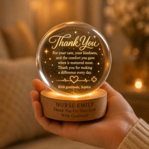 Puede incluir: Una luz nocturna esférica de cristal sobre una base de madera. El cristal presenta el texto: Thank You, For your care, your kindness, and the comfort you gave when it mattered most. Thank you for making a difference every day. With gratitude, Sophia. La base dice: NURSE EMILY, Thank You For Your Care, With Gratitude.