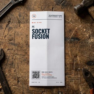 May include: A white pocket reference guide titled "PE Socket Fusion" with the text "The Apprentice's Edge." The guide includes a QR code and the text "More Cheat Sheets." Tools like wrenches and hammers surround the guide on a wooden surface.