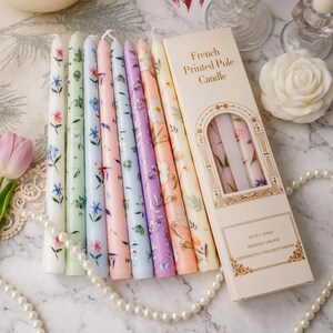 May include: A set of eight taper candles featuring various floral patterns in pastel colours, including white, green, blue, pink, lavender, and peach. The packaging box is labelled French Printed Pole Candle and Set of 2 10 inch.
