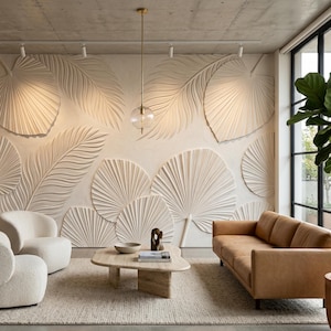 May include: A living room featuring a large off-white wall with a three-dimensional palm leaf relief pattern, two cream-colored textured armchairs, a tan leather sofa, a light-colored stone coffee table, and a tall green potted plant.