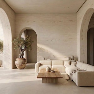 May include: A neutral-toned living room with a large, cream-colored sectional sofa, a wooden coffee table, and a decorative vase. An olive tree in a large pot sits near an arched doorway. The walls and floors are a light beige.