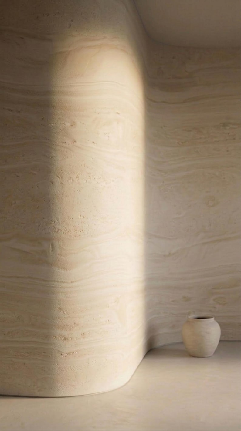 May include: A minimalist interior scene featuring a light-toned, curved wall with a natural, layered texture. A small, off-white ceramic vase sits on the floor. The scene is bathed in soft, natural light, creating a serene and artistic ambiance.