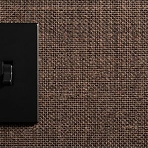 May include: A matte black rectangular light switch with a single vertical toggle lever, mounted flush against a dark brown textured fabric wall covering that features a prominent woven burlap-like grid pattern across the entire surface area.