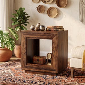 May include: A square wooden side table with a dark brown finish and a hollow center compartment. The top surface holds three small ceramic vases and two stacked books. Inside the lower open shelf sits a small wooden box and a gold-toned clock.