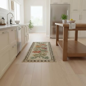 May include: A rectangular runner rug featuring a central botanical print of red, orange, and yellow roses with green foliage on a cream background, framed by a dark geometric border pattern, positioned on a light-coloured wooden kitchen floor.
