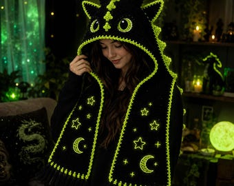 May include: Black crochet dragon hood and scarf set with neon green trim and accents. The hood features dragon eyes and spikes, while the scarf is adorned with glowing stars and crescent moons. The set includes a fringe at the bottom.