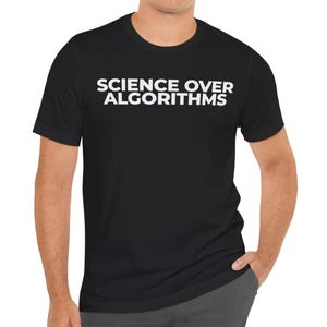 May include: Black t-shirt with the white text "SCIENCE OVER ALGORITHMS" across the chest. The shirt has short sleeves and a crew neck. The person is wearing gray pants.