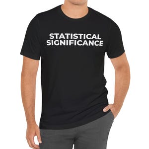 Può includere: T-shirt nero con la scritta "STATISTICAL SIGNIFICANCE" stampata in lettere bianche sul petto. La maglietta è a maniche corte e sembra essere realizzata in un materiale morbido.