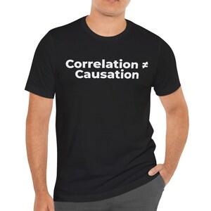 May include: Black t-shirt with the white text "Correlation ≠ Causation". The shirt is a crew neck style and appears to be made of a soft material. The text is centered on the chest.