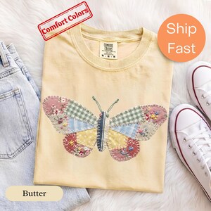 Puede incluir: Una camiseta color amarillo mantequilla con un gráfico de mariposa grande hecho de varios parches de tela en cuadros verdes, tartán azul, lunares amarillos y patrones florales con costuras visibles. La camiseta tiene una etiqueta Comfort Colors.