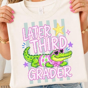 Könnte beinhalten: Cremefarbenes T-Shirt mit dem pinkfarbenen Text "Later Third Grader", das ein Cartoon-Alligator mit herzförmiger Sonnenbrille und einem Argyle-Pullover zeigt. Das Design umfasst Sterne und vertikale Streifen.