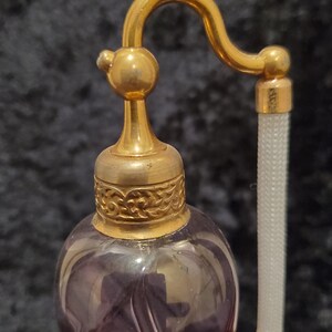 May include: A vintage glass perfume bottle with a gold-toned metal top and a long, thin, white spray nozzle. The bottle is a deep purple color and has a swirling pattern.