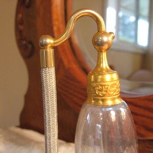 May include: A gold-colored glass perfume bottle with a decorative stopper and a gray cord.