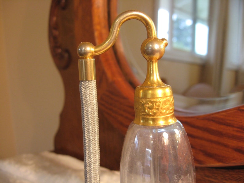 May include: A gold-colored glass perfume bottle with a decorative stopper and a gray cord.