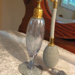 May include: A vintage glass perfume bottle with a gold top and a gray tassel. The bottle has a clear glass body and a silver base.