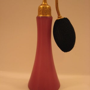 May include: A pink glass perfume bottle with a gold top and a black atomizer. The bottle has a slender, elegant shape.