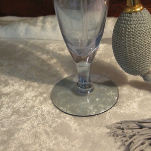 May include: A blue glass perfume bottle with a gray fabric atomizer and tassel. The bottle has a wide base and a narrow neck. The atomizer has a gold top.