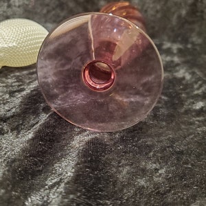 May include: The bottom of a clear glass vase with a pink hue. The vase has a wide base and a narrow neck.