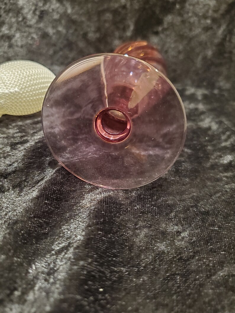 May include: The bottom of a clear glass vase with a pink hue. The vase has a wide base and a narrow neck.
