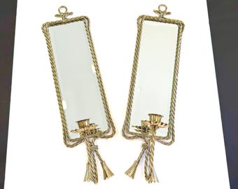 May include: A pair of rectangular wall mirrors with gold-toned metal frames featuring a twisted rope design. Each mirror includes a candle holder at the bottom, a small hanging loop at the top, and decorative metal tassels hanging below.