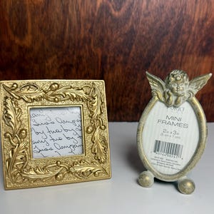 May include: A square gold-toned picture frame with an embossed leaf pattern and an oval gold-toned picture frame topped with a cherub figure. The oval frame includes a product label reading FURIO MINI FRAMES 2 in x 3 in (5 cm x 7 cm).
