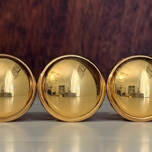 May include: A set of five polished brass spherical cabinet knobs arranged in a horizontal row. Each knob features a smooth, reflective, gold-toned metallic surface with a rounded dome shape and a circular base, showcasing a bright, uniform finish.