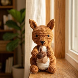 May include: A handmade crochet squirrel doll in shades of brown and white, holding a brown acorn. The squirrel has black eyes and a black nose. The doll is sitting on a wooden surface near a window.