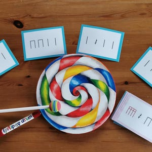 Puede incluir: Un tambor colorido con forma de piruleta con un palo blanco y el texto "Lip Pop Drum". Varias tarjetas blancas con bordes azules, cada una con notación musical, rodean el tambor. El tambor tiene remolinos rojos, amarillos, azules y verdes.