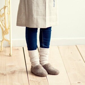 Pode incluir: Um par de pantufas de l&atilde; marrom com uma bainha de malha branca. As pantufas s&atilde;o usadas por uma pessoa que usa jeans azul e uma saia de linho marrom claro.
