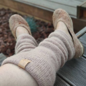 May include: A pair of light brown fuzzy leg warmers with a small leather tag that says "Natur" on it. The leg warmers are worn with light brown slippers.