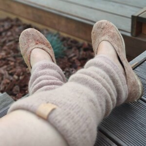 May include: A pair of brown felt slippers with a light brown knitted leg warmer. The slippers are worn and have a worn look.