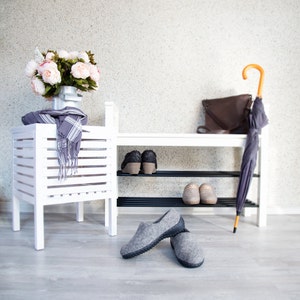 Puede incluir: Zapatero de madera blanco con dos estantes, una bufanda gris, un ramo de flores rosas y dos pares de zapatillas grises. Un bolso de cuero marr&oacute;n y un paraguas est&aacute;n en el estante superior.