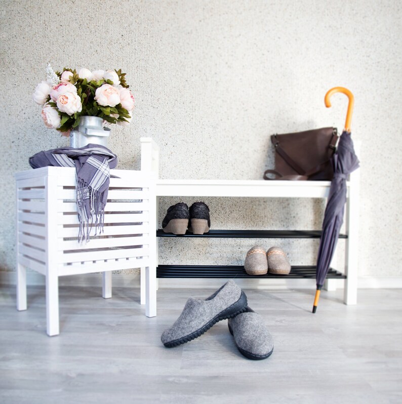 Puede incluir: Zapatero de madera blanco con dos estantes, una bufanda gris, un ramo de flores rosas y dos pares de zapatillas grises. Un bolso de cuero marr&oacute;n y un paraguas est&aacute;n en el estante superior.