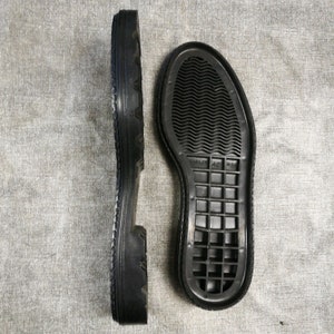 May include: Two black rubber shoe soles. The sole on the left has a textured tread pattern. The sole on the right has a grid pattern and the text "STANLEY 42 M6A".