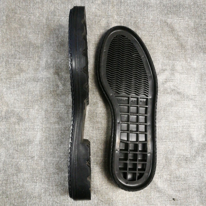 May include: Two black rubber shoe soles. The sole on the left has a textured tread pattern. The sole on the right has a grid pattern and the text "STANLEY 42 M6A".
