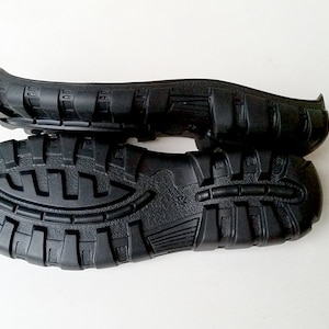 May include: A pair of black rubber shoe soles with a textured tread pattern. The soles are stacked on top of each other.