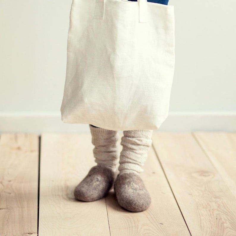 Pode incluir: Uma bolsa tote de lona branca com um par de pantufas de l&atilde; cinzas. As pantufas est&atilde;o gastas e t&ecirc;m um aspeto ligeiramente desgastado.