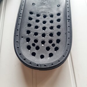 May include: Black rubber insole with a grid of small holes. The insole is designed to provide support and ventilation for the foot.