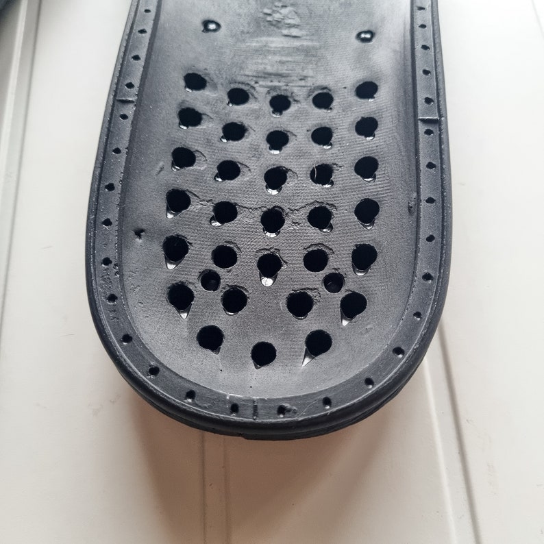 May include: Black rubber insole with a grid of small holes. The insole is designed to provide support and ventilation for the foot.