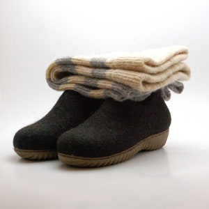May include: A pair of black felt boots with a brown rubber sole. The boots are topped with a folded pair of white and gray striped socks.