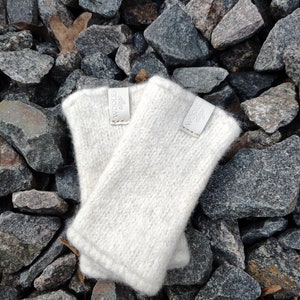 May include: Two white knitted fingerless gloves with a white label that says "WOOLLEN 420F" on each glove. The gloves are on a bed of gray rocks.